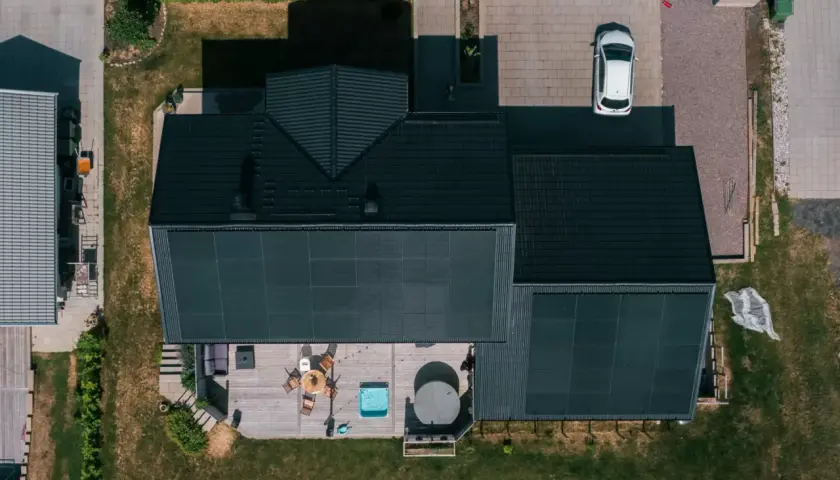 Tak med solceller fångar solens energi. Ett modernt hus med altan, bubbelpool och en vit bil på uppfarten.