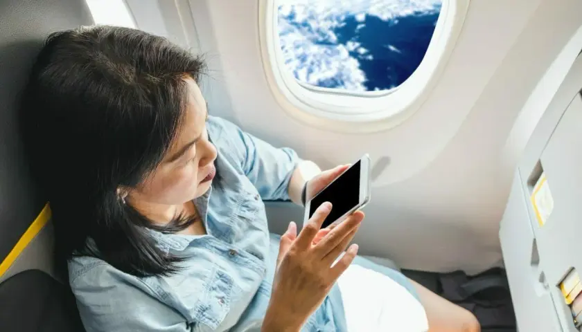 Kobieta z telefonem siedzi przy oknie w samolocie Ryanair, podziwiając widok chmur.