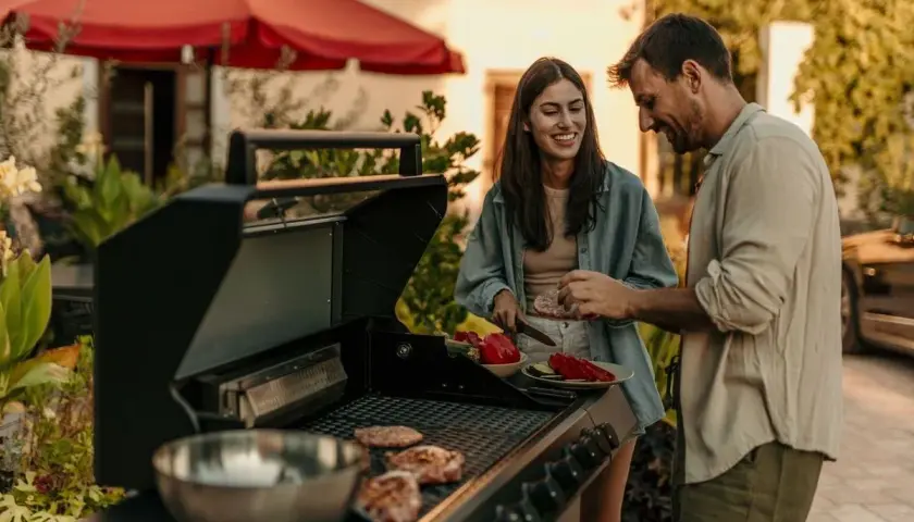 Un couple prépare une soiree barbecue party. Des steaks cuisent sur le grill pendant qu'ils coupent des légumes.