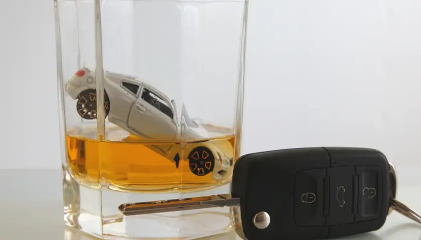 Miniaturowy samochód w szklance z bursztynowym płynem, obok kluczyki. Zastanawiasz się, ile ml ma shot wódki, ale pamiętaj: jazda po alkoholu to ryzyko.
