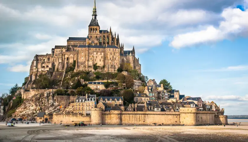 Mont-Saint-Michel, średniowieczny zamek na wyspie we Francji, z widokiem na piaszczyste wybrzeże.