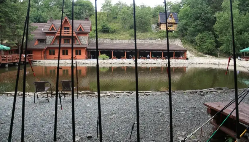 Wędki nad jeziorem z drewnianymi domkami i zadaszoną restauracją w tle.