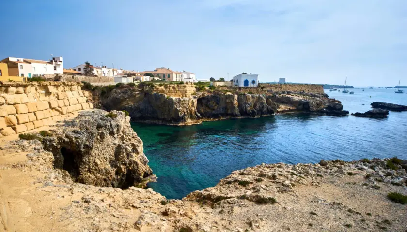 Explora la isla de Tabarca: casas blancas sobre acantilados rocosos, aguas cristalinas y barcos en el horizonte. Un lugar para descubrir.