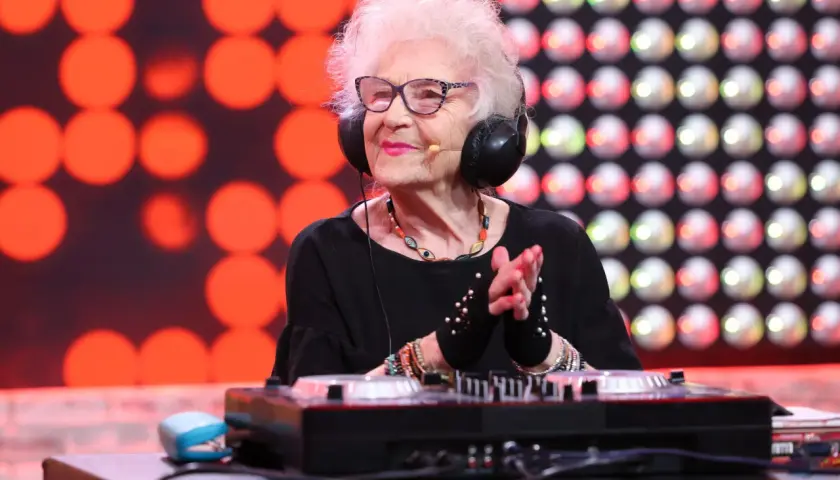 DJ Wika w słuchawkach, z uśmiechem na twarzy, miksuje muzykę. W tle czerwone i białe światła.