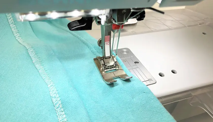 A double needle stitches a hem on turquoise fabric. Most sewing machines can use a double needle with the right setup.