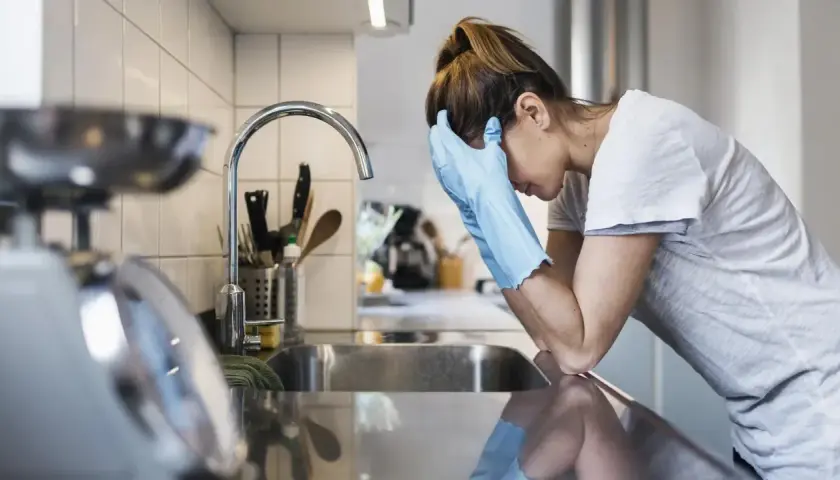 Kobieta w rękawiczkach opiera się o zlew, wyraźnie przygnębiona. Mizofobia utrudnia jej codzienne czynności.