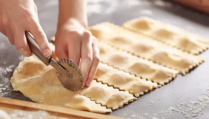 Hände schneiden mit einem Teigrädchen frische Ravioli. So einfach ist ravioli selber machen!