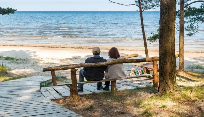 Para odpoczywa na ławce przy plaży, ciesząc się widokiem morza. Idealne miejsce na regenerację w sanatorium nad morzem.