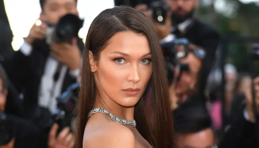 Bella Hadid con un elegante side part, luciendo un collar de diamantes y rodeada de fotógrafos.