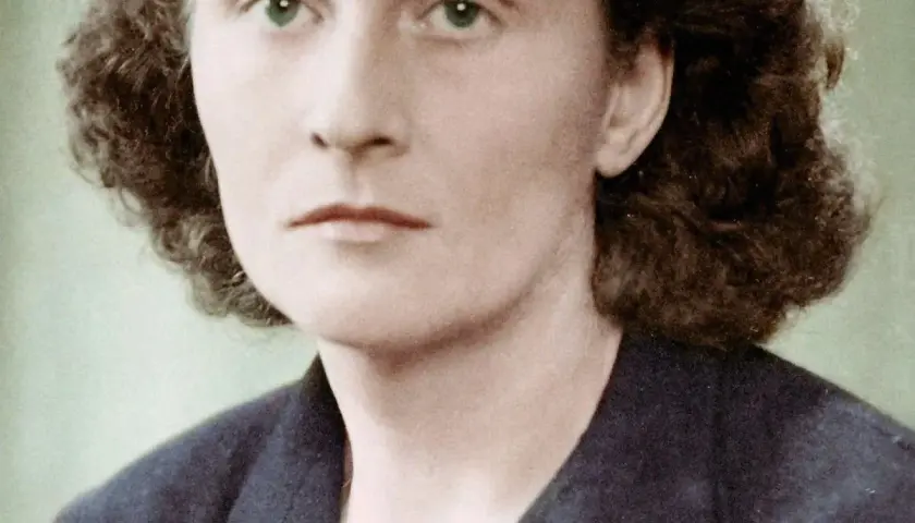 Portret Catherine Dior z zielonymi oczami i kręconymi włosami, w ciemnej marynarce.