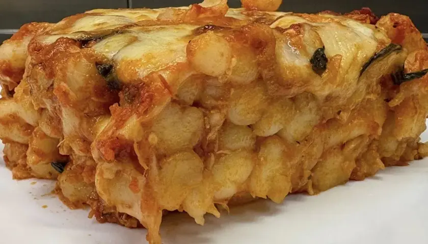 Porzione generosa di gnocchi al forno, dorati e filanti, con sugo e formaggio fuso.
