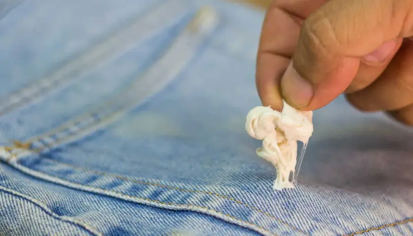Maintenant, découvrez comment enlever du mastic sur un vêtement. Une main retire une boule de chewing-gum collante d'un jean bleu.