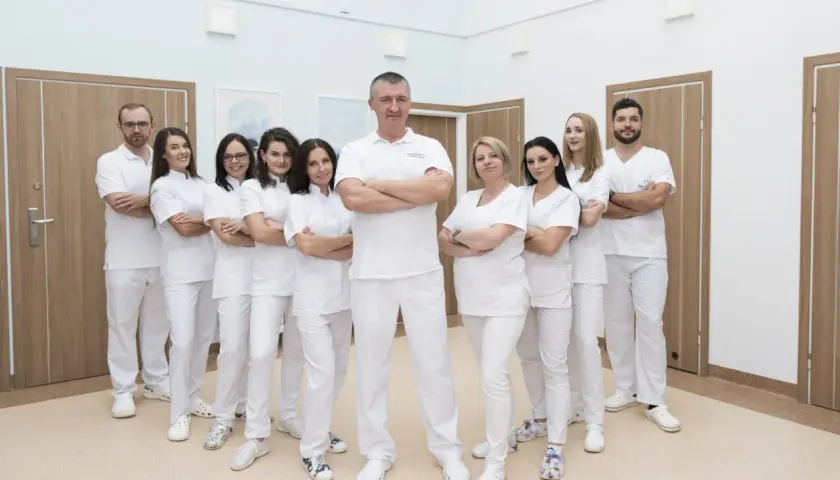 Zespół stomatologów w białych uniformach stoi w rzędzie, z rękami skrzyżowanymi na piersi.