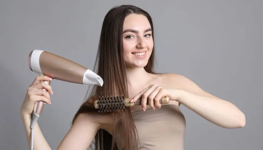 Kobieta suszy i modeluje włosy okrągłą szczotką i suszarką.