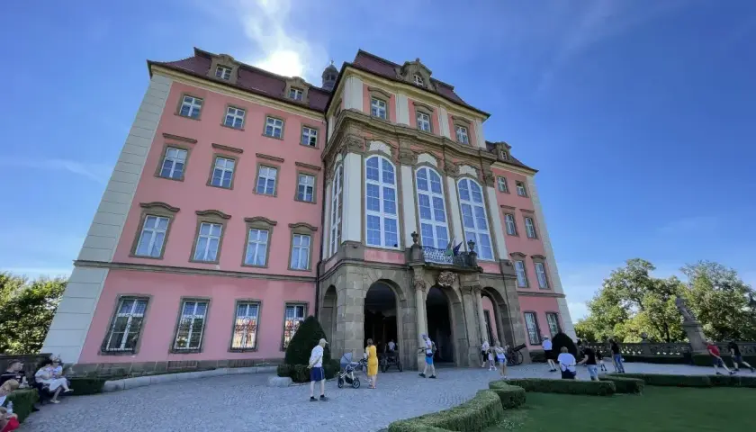 Zamek Książ, malowniczo położony, łatwy dojazd PKP. Turyści zwiedzają barokową budowlę w słoneczny dzień.