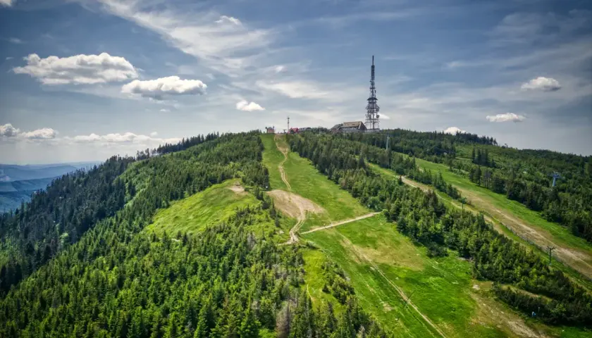 Widok na zielone **beskidzkie szczyty** z wieżą telekomunikacyjną na szczycie.
