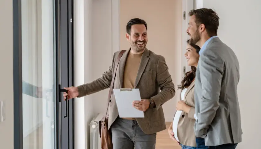 Agent ouvrant une porte à un couple, discutant des risques à acheter un bien loué.