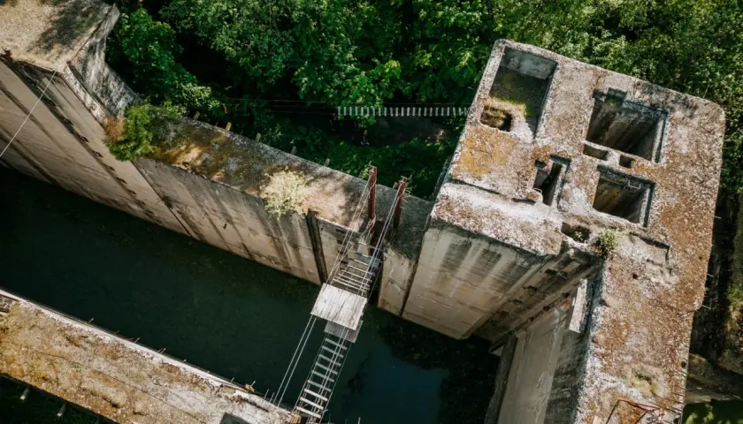 Widok z lotu ptaka na betonową śluzę Leśniewo Górne, otoczoną bujną zielenią. Woda w kanale jest ciemna, a na budowli widać ślady czasu.