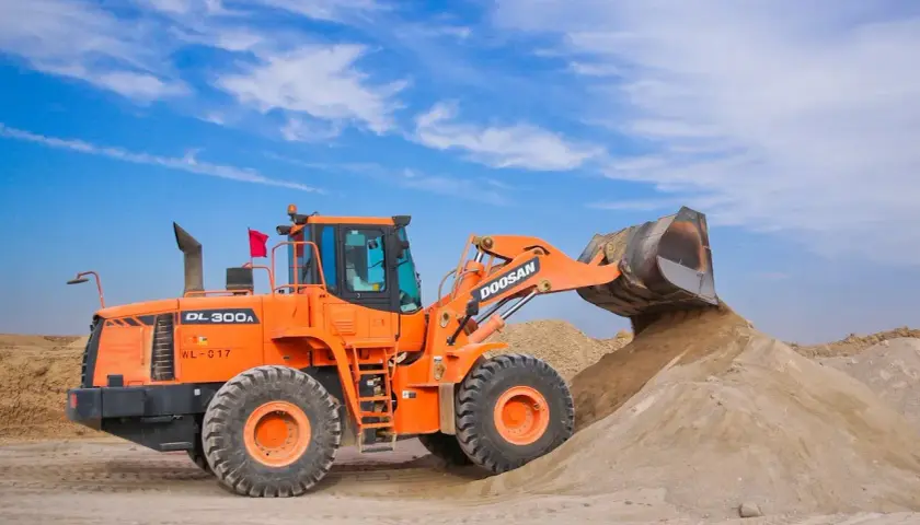 Pomarańczowa ładowarka Doosan DL300A zasypuje kopiec piasku, który może posłużyć jako żwir do betonu.