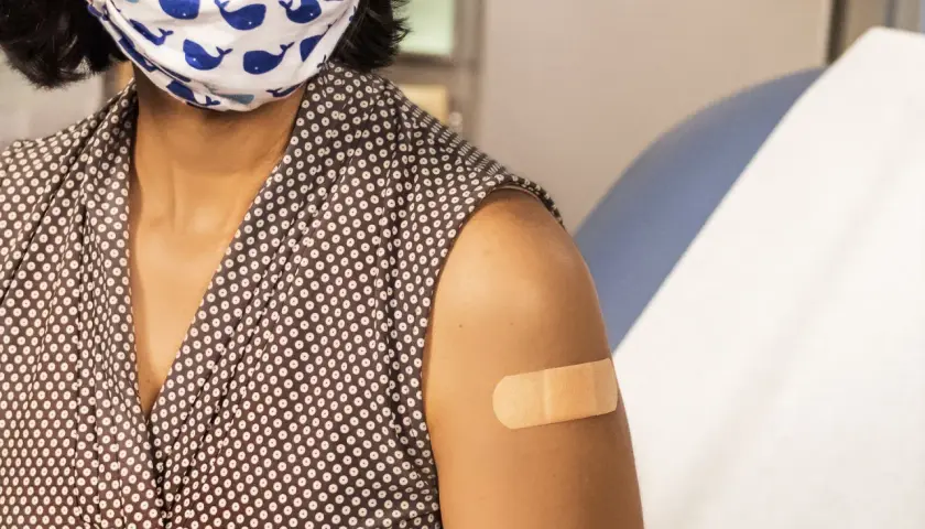 Osoba z maską na twarzy i plastrem na ramieniu po szczepieniu. Choć hpv szczepionka skutki uboczne są rzadkie, warto być świadomym.