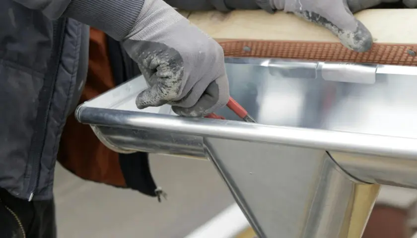 Hand mit Handschuh dichtet Dachrinne mit Werkzeug ab.