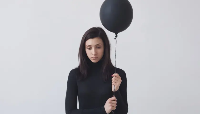 Donna con palloncino nero, espressione malinconica. Potrebbe rappresentare l'anedonia significato, la perdita di piacere.