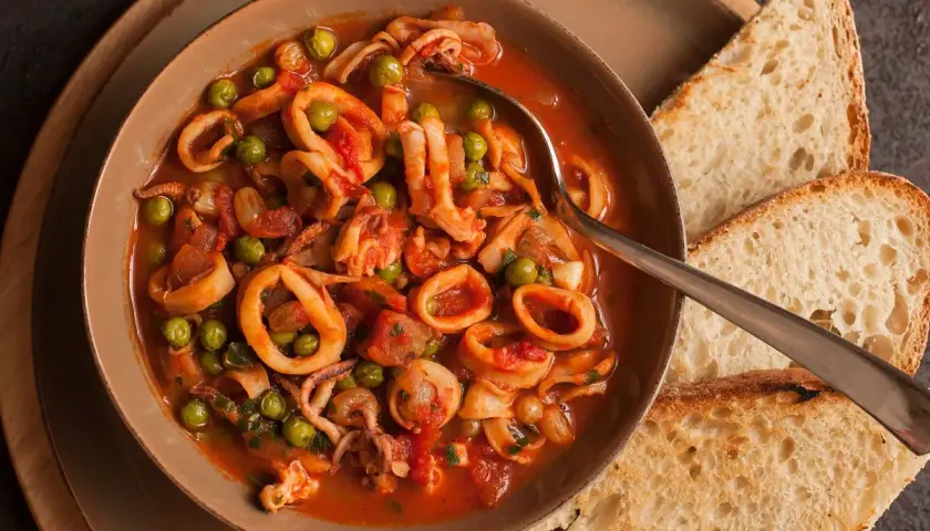 Calamari al sugo con piselli, un piatto saporito servito in una ciotola con pane tostato.