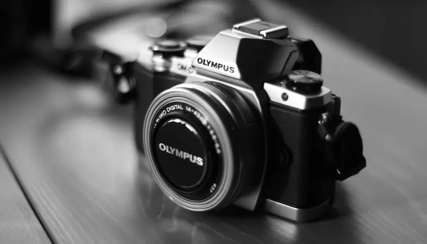 Prześwietlone zdjęcie aparatu Olympus OM-D. Srebrno-czarny korpus i obiektyw z napisem "OLYMPUS".