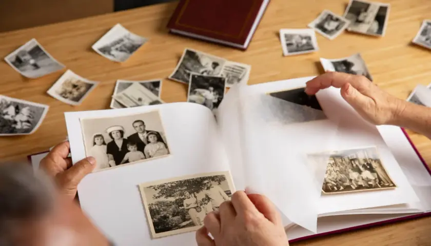 Wspomnienia wracają podczas wklejania zdjęć do albumu. Na stole leżą stare fotografie, a ręce starannie układają je na białych kartach.