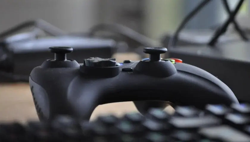 Czarny kontroler do gier leży na klawiaturze, gotowy do akcji. W tle widać monitor, jakby tworzył **steam cloud** dla wirtualnych światów.