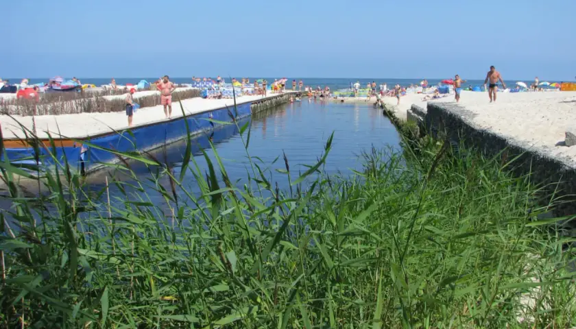 Słoneczny dzień nad kanałem w Karwi. Ludzie odpoczywają na plaży, a woda przyciąga do kąpieli. To jedna z wielu atrakcji w okolicy.