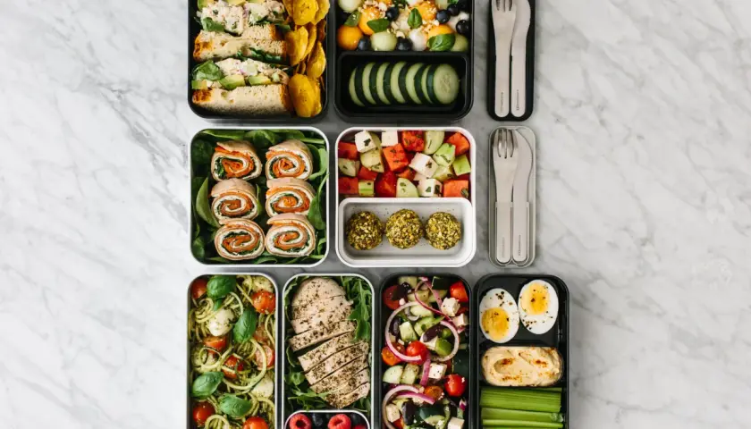 A colorful bento box diet spread with sandwiches, fruit salad, chicken, pasta, and snacks, perfect for a healthy lunch.