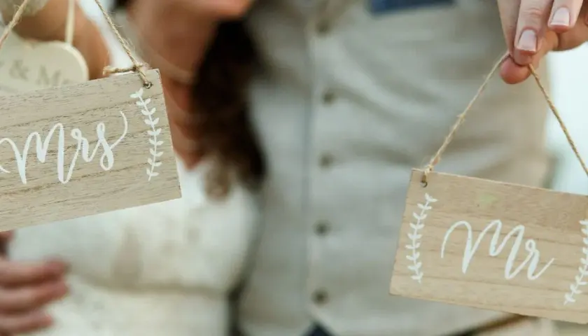 Para Młoda trzyma tabliczki "Mr" i "Mrs", symbolizujące zmianę nazwiska po ślubie.