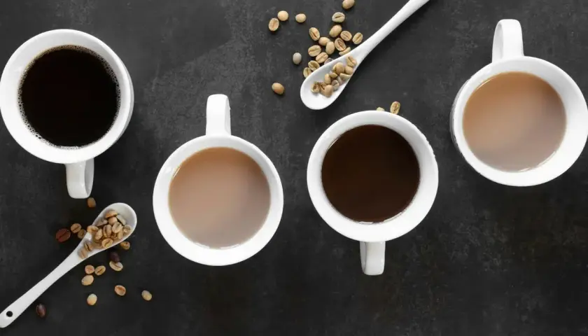Vier Tassen Kaffee, zwei schwarz, zwei mit Milch, und Löffel mit Kaffeebohnen. Ein gemütlicher Tee-Teein-Moment.