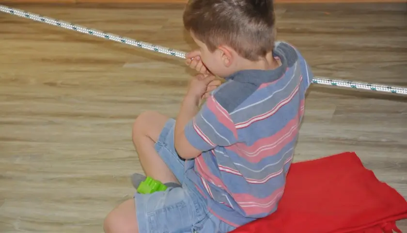 Chłopiec ćwiczy obniżone napięcie mięśniowe w jamie ustnej, bawiąc się sznurkiem.