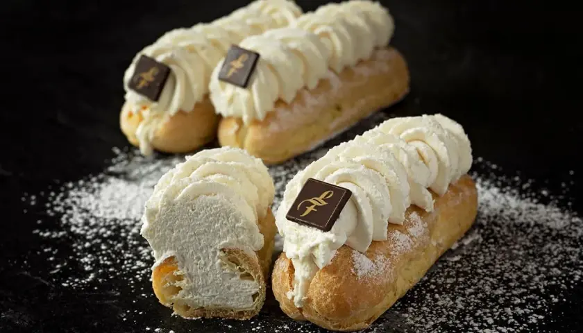 Trois éclairs chantilly généreusement garnis de crème fouettée, ornés d'un carré de chocolat, saupoudrés de sucre glace.