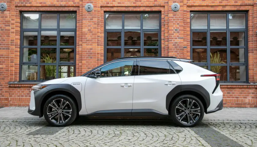 Biały Toyota bZ4X elektryczny SUV stoi na brukowanej ulicy przed ceglanym budynkiem z dużymi oknami.
