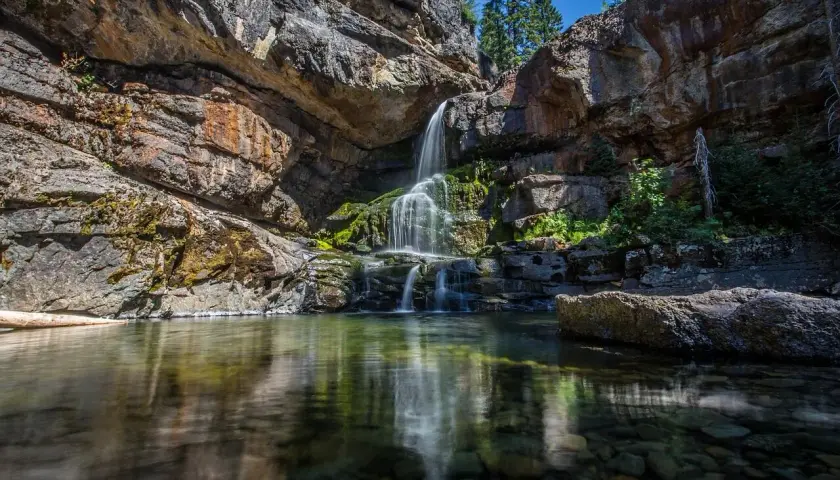 Cascadas en León, agua cristalina cae sobre rocas cubiertas de musgo, reflejándose en un estanque sereno.
