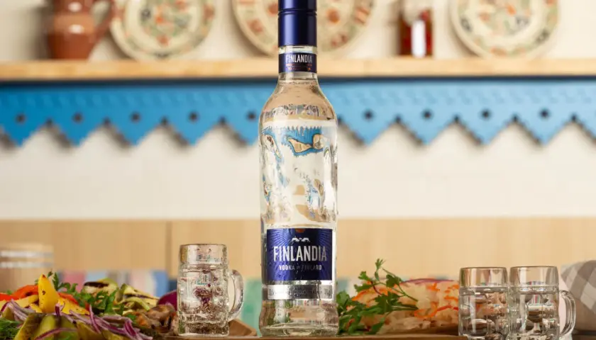 Butelka wódki Finlandia z kieliszkami i przekąskami na stole.