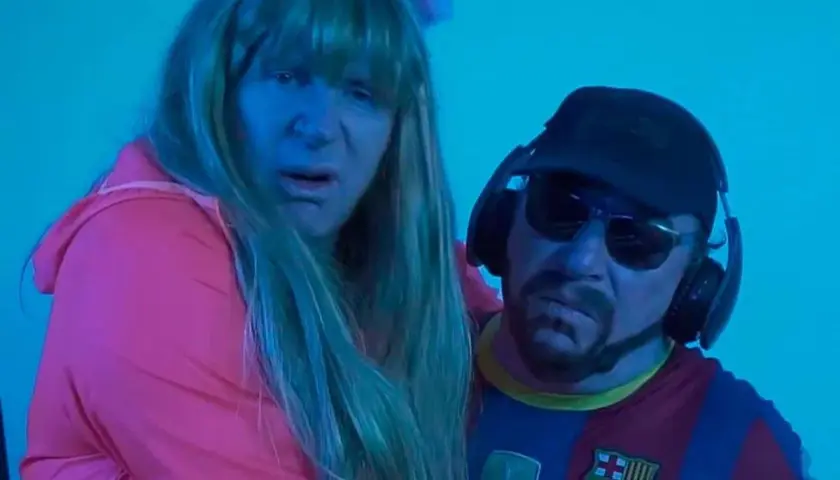 Dos personas con peluca y gorra, una con camiseta del Barça, parecen estar cantando la letra de "el pantalon".