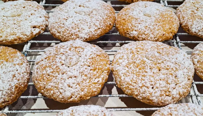 Biscotti con farina di mandorle, cosparsi di zucchero a velo, riposano su una griglia.