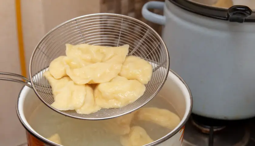 Gotowanie pierogów: cedzak z pierogami nad garnkiem z wrzącą wodą. Tak, pierogi wrzuca się do gotującej wody.