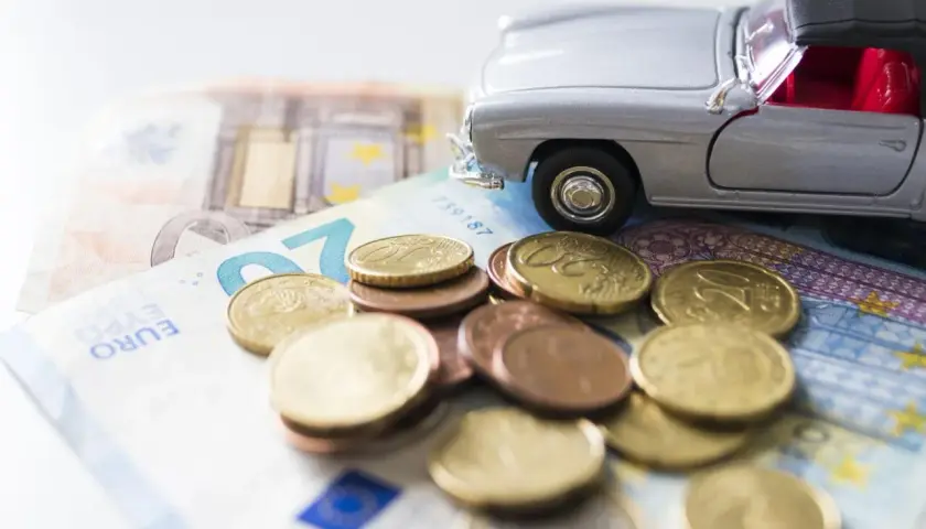 Modellino d'auto su banconote e monete euro. Un promemoria dei costi di gestione, incluso il **super bollo auto**.