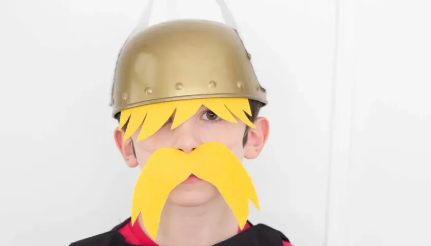 Niño con disfraz casero de Astérix y Obélix, luciendo casco dorado y bigote amarillo.