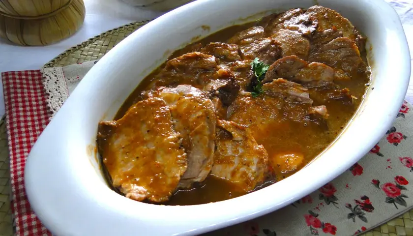 Arrosto di maiale morbido con sughetto in pentola, pronto per essere gustato.