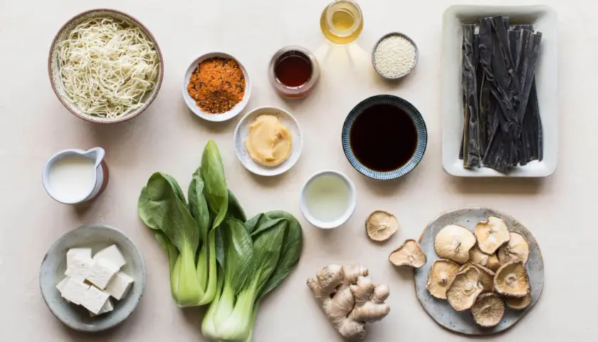 A collection of ingredients for a Japanese meal, including noodles, bok choy, tofu, ginger, dried mushrooms, and various Japanese sauces and seasonings.