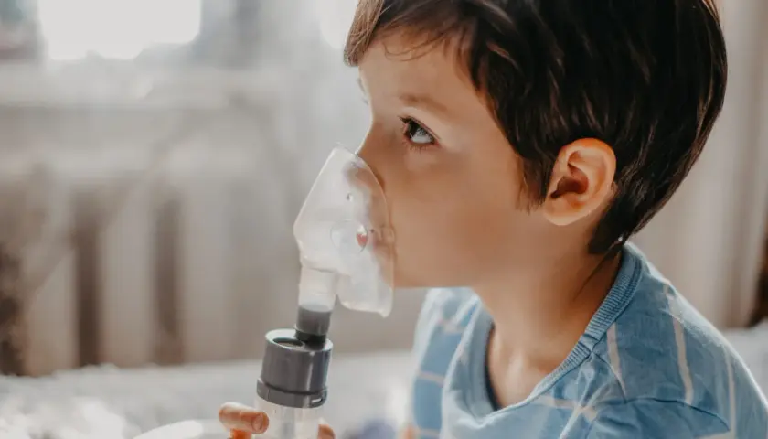 Chłopiec z maską inhalatora na twarzy, wdycha sól fizjologiczną do inhalacji.