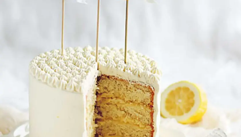 Tårta med fluffig frosting och lager av saftig sockerkaka fylld med syrlig lemon curd. En citronskiva ligger bredvid.