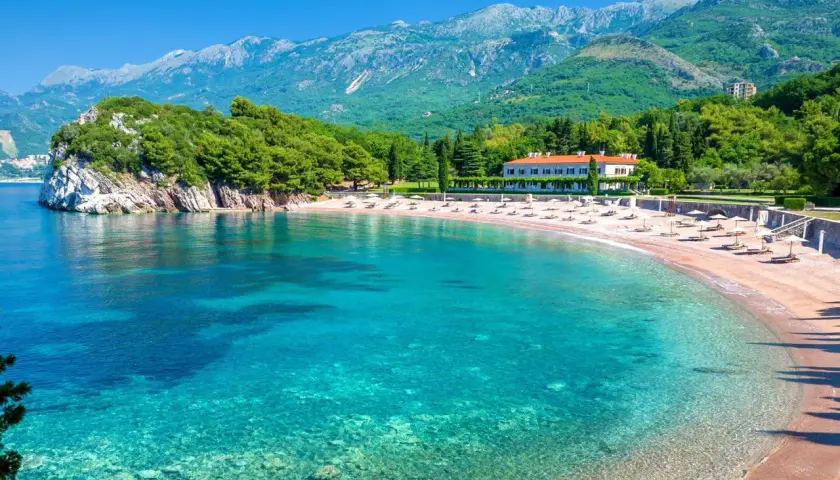 Malownicza zatoka z turkusową wodą i piaszczystą plażą. W tle hotel i zielone wzgórza. Idealne czarnogóra plaże na wakacje.