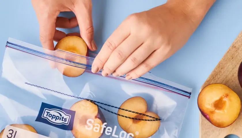 Hände legen Pflaumenhälften in einen Toppits SafeLoc Beutel zum Einfrieren. So bleiben die Früchte lange frisch.
